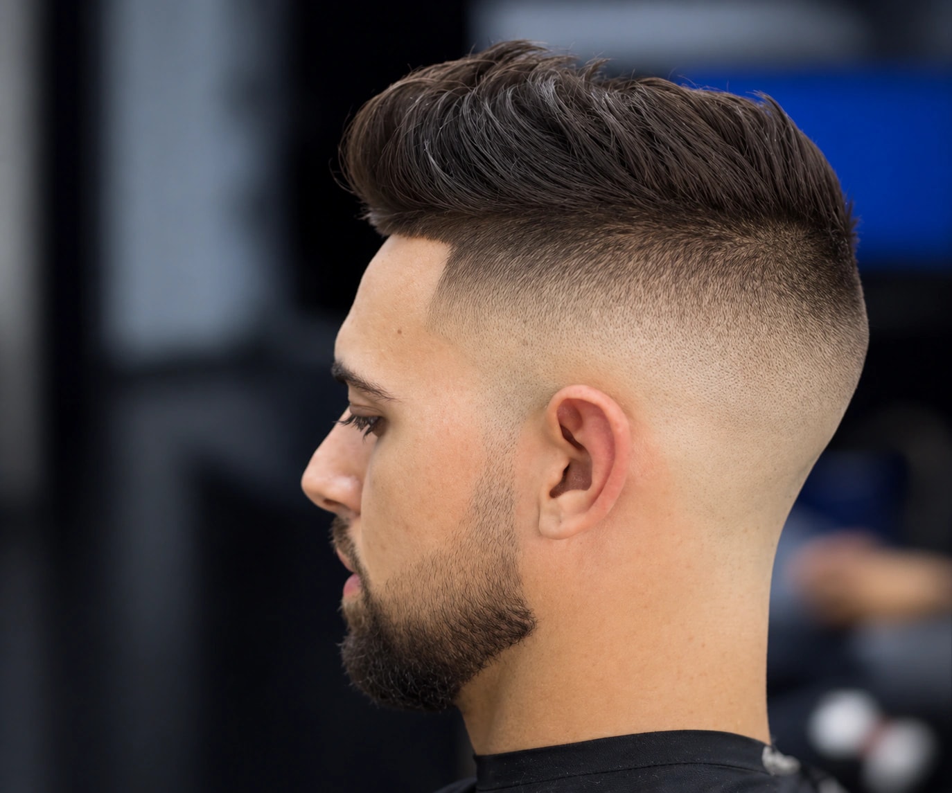 High fade with a pompadour on top and a short, neatly lined beard